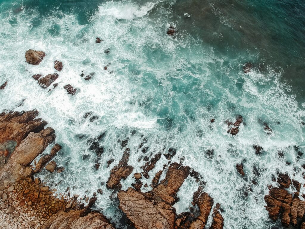 Aerial view of rugged coastal rocks with turquoise sea waves creating textured natural wallpaper