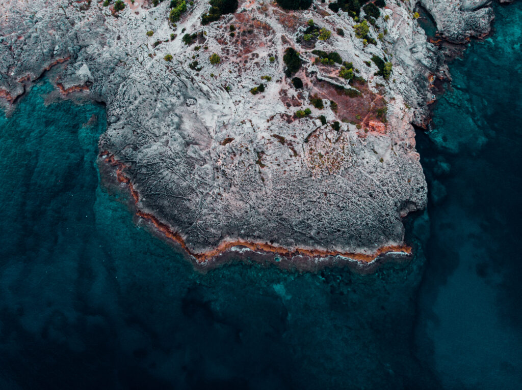 Aerial view of rugged rocky shore with textured stones and turquoise ocean waves background wallpaper