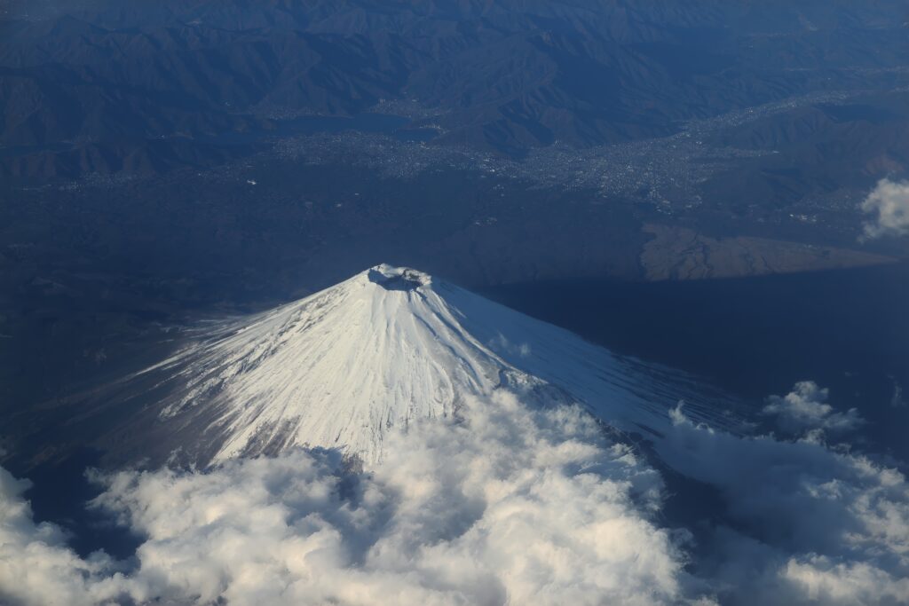 Aerial view of snow-capped volcanic mountain peak with clouds and shadowed valleys wallpaper