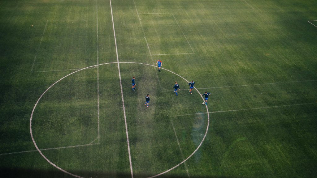 Aerial view of five men in blue training kits playing soccer on lush green pitch wallpaper background