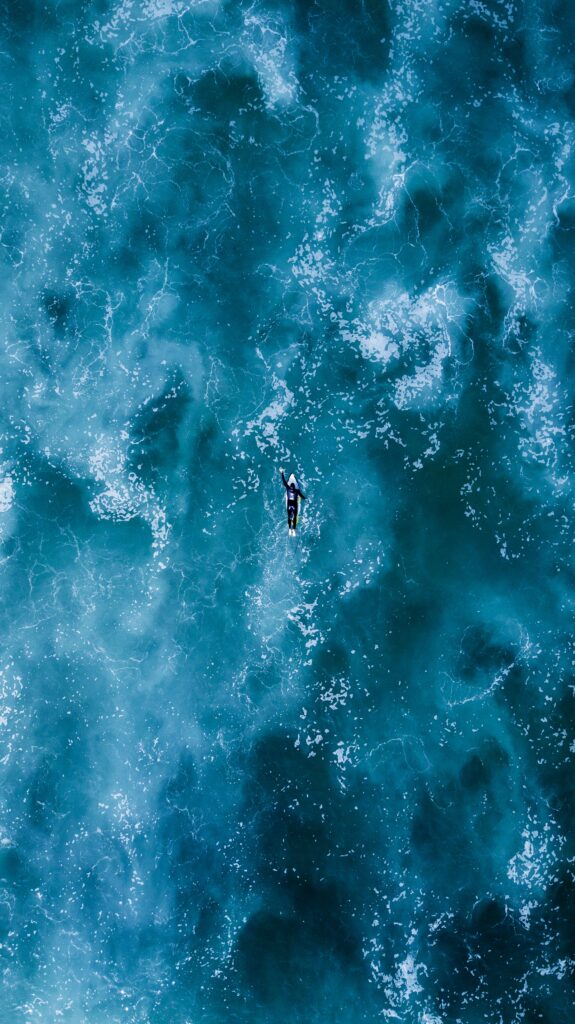 Aerial view of surfer riding vibrant blue ocean waves with swirling foamy patterns wallpaper
