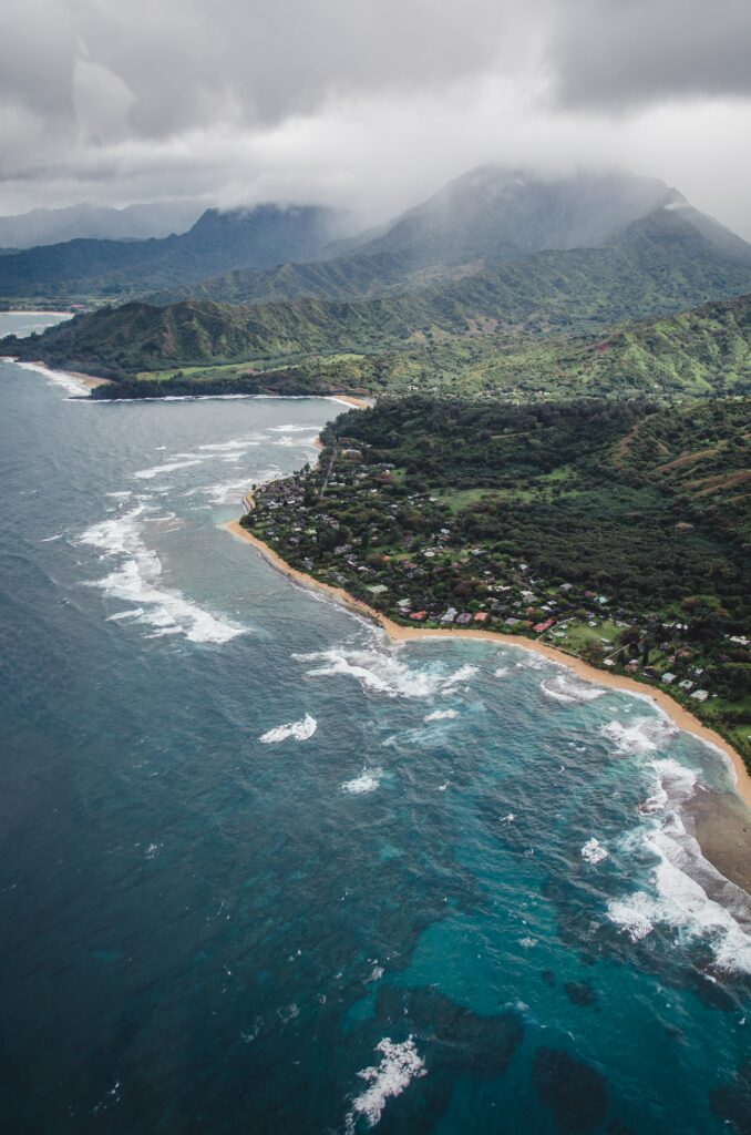 Aerial view of tropical island village with emerald hills and turquoise ocean waves wallpaper