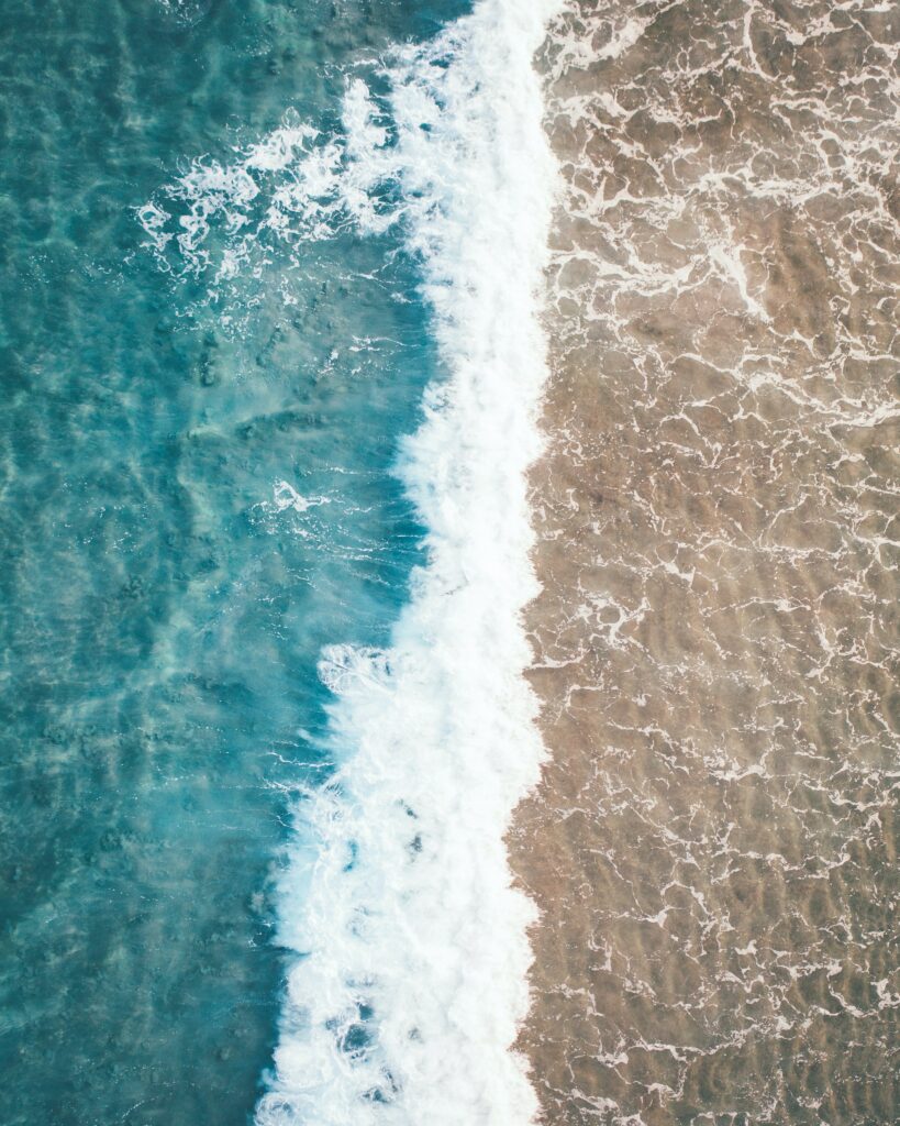 Aerial view of turquoise waves crashing onto sandy shore vibrant beach wallpaper background