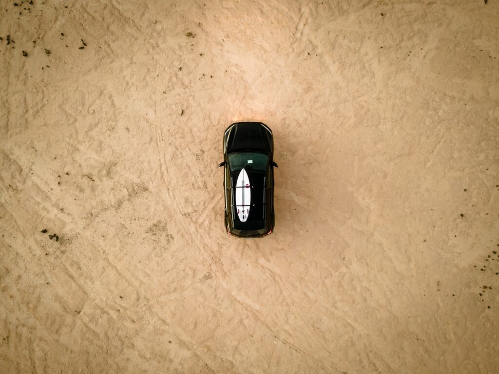 Aerial View: Black Car with Surfboard at Sandy Beach Adventure Wallpaper