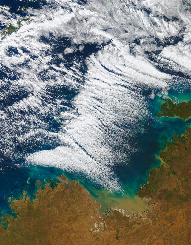 Aerial view of rust-colored mainland and vibrant blue green ocean with dynamic clouds wallpaper
