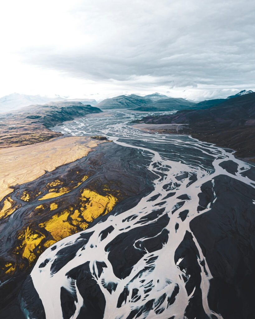 Aerial view of winding river through dramatic mountains with yellow patches and moody sky wallpaper