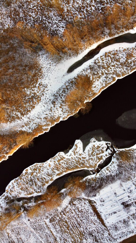 Aerial view of winding river through snow-dusted forest with brown trees winter landscape wallpaper