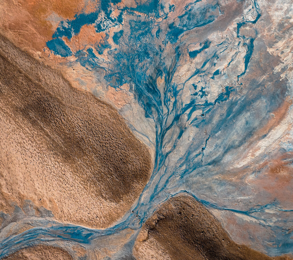 Aerial view of winding river branching across rugged earthy banks with vibrant blue and warm tones Wallpaper