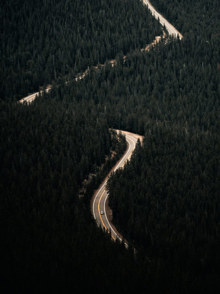 Aerial view of winding forest road with a lone car highlighting serene natural landscape wallpaper