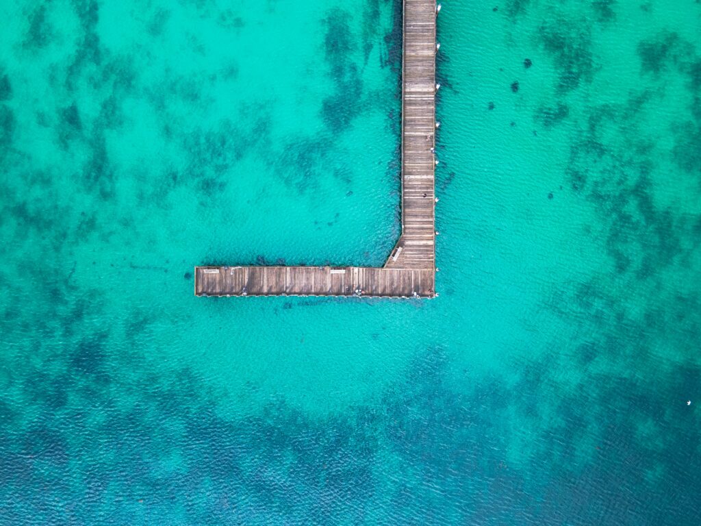 Aerial view of wooden pier over turquoise ocean with dark patches creating coastal calm wallpaper
