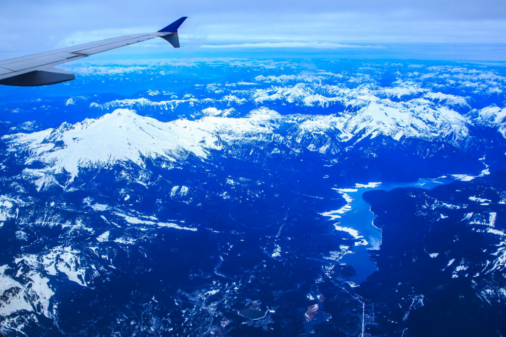 Aerial view of airplane wing over snow-covered Washington mountains with blue sky and lakes Wallpaper