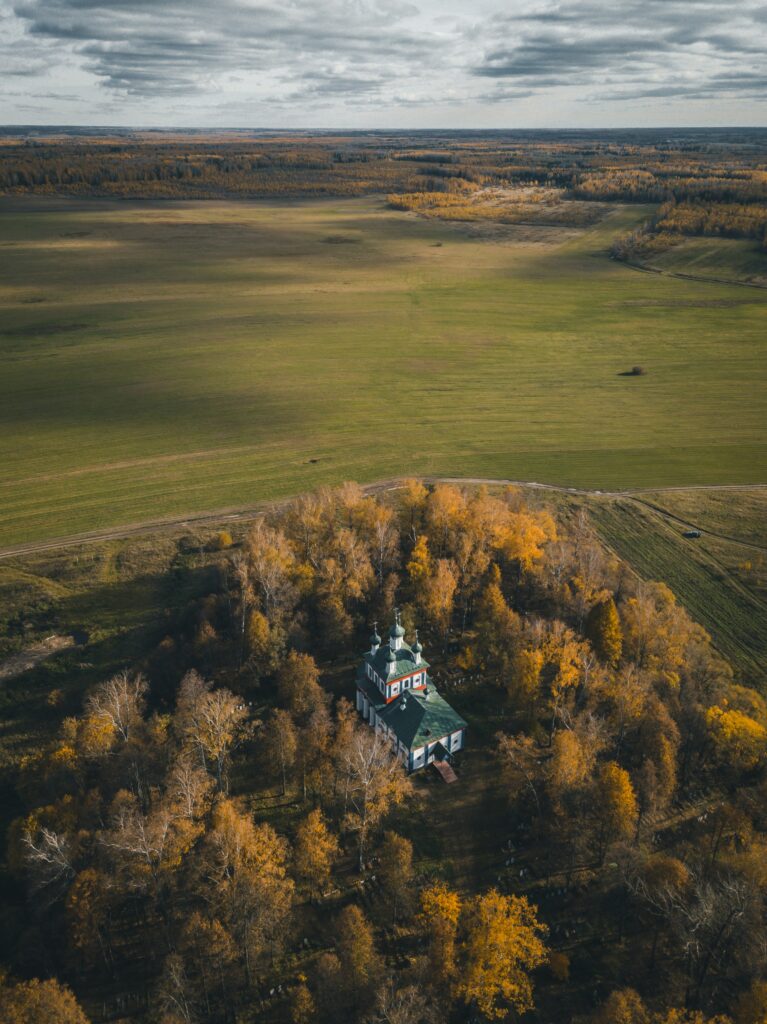 Aerial view of charming church amid autumn trees and open fields under dramatic cloudy sky Wallpaper