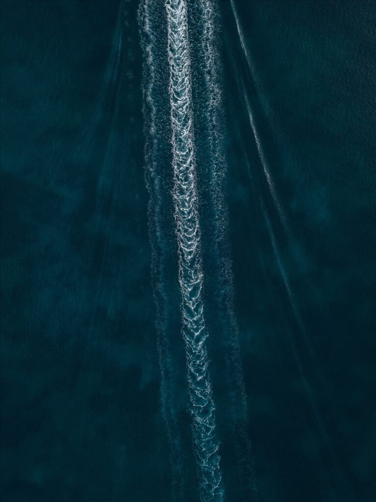 Aerial view of deep blue sea with foamy white ripples from a boat on calm water ocean wallpaper