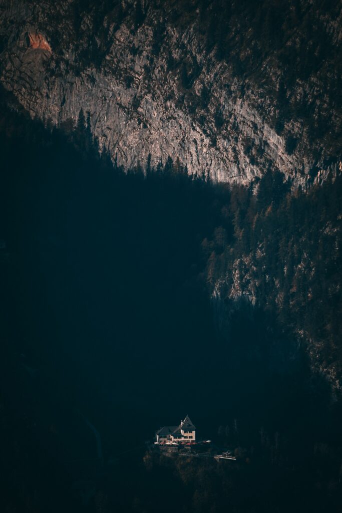 Aerial view of isolated house at mountain base with dramatic shadows and moody landscape background Wallpaper