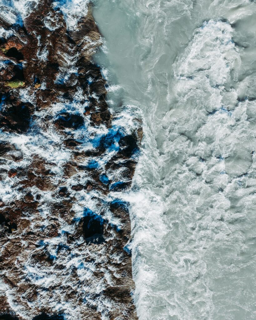 Aerial view of powerful waves crashing on rugged rocks with deep blue sea and white surf wallpaper