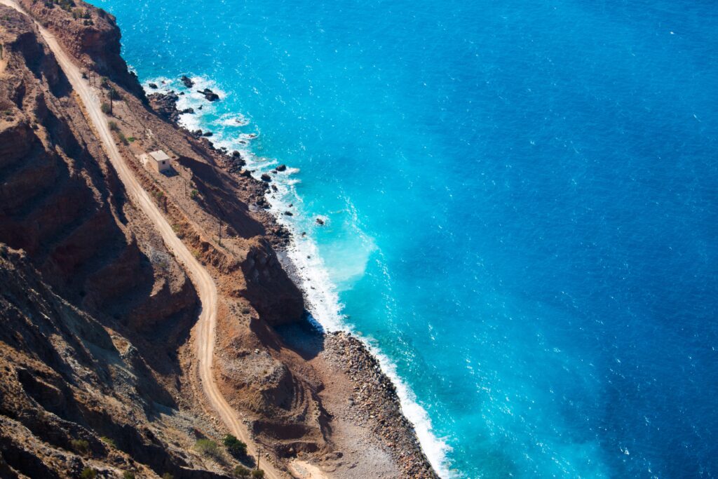 Aerial view of rugged coastal road winding along cliffs beside vibrant turquoise sea waters wallpaper
