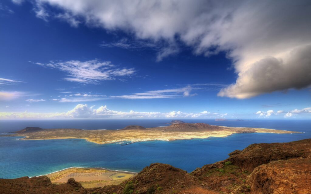 Aerial view of vibrant island with rugged coastline clouds and deep blue ocean wallpaper background