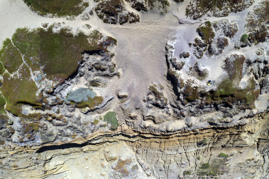 Aerial view of rugged rock relief with layered geological formations and sparse vegetation background Wallpaper