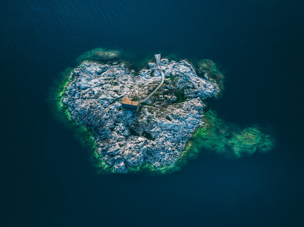 Aerial view of small Swedish island with rocky terrain winding path solitary building and green shallows Wallpaper