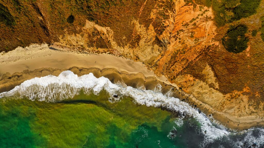 Aerial view of vibrant coastal wallpaper with turquoise sea foamy surf golden beach and rust cliffs