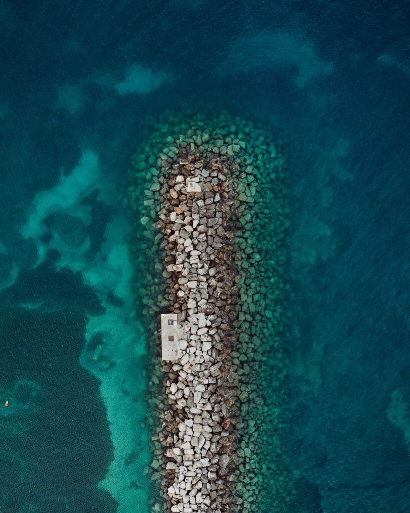 Aerial view of stone breakwater extending into vibrant turquoise and deep blue sea waters wallpaper