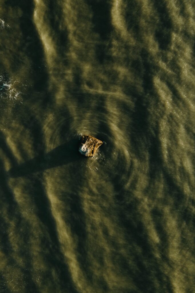 Aerial view of a stone in water with soft waves and earthy tones creating peaceful texture Wallpaper