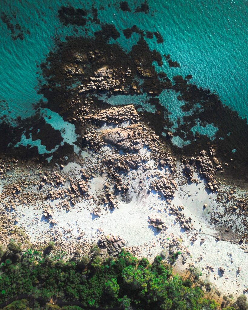 Aerial view of turquoise ocean meeting rocky shore with sandy beach and lush green coastline Wallpaper