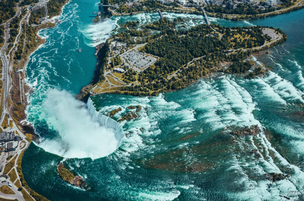Aerial view of vibrant turquoise waterfalls cascading over rocky cliffs surrounded by lush greenery Wallpaper