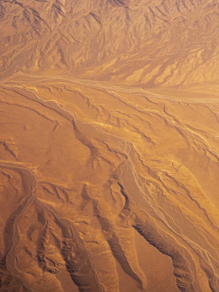 Aerial view of desert landscape with intricate wind-eroded patterns in warm orange and brown tones Wallpaper