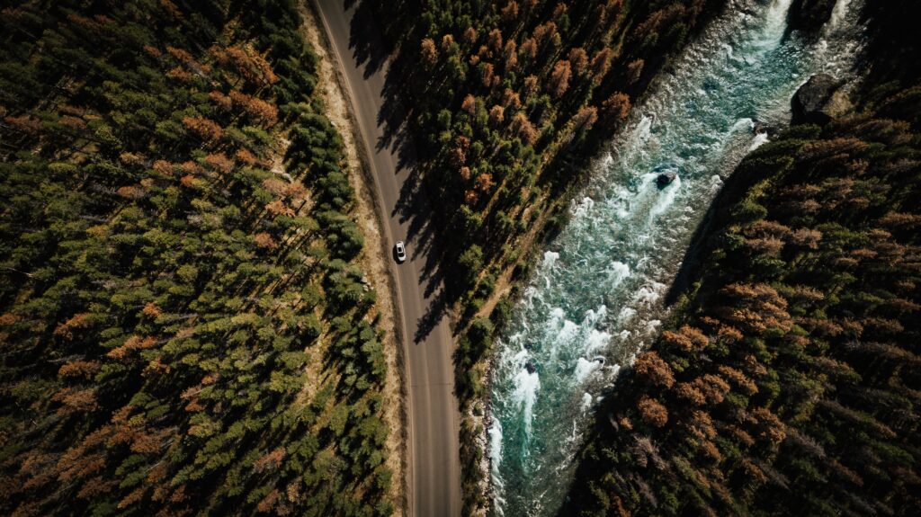 Aerial view of winding road through dense forest beside rushing river nature travel wallpaper background