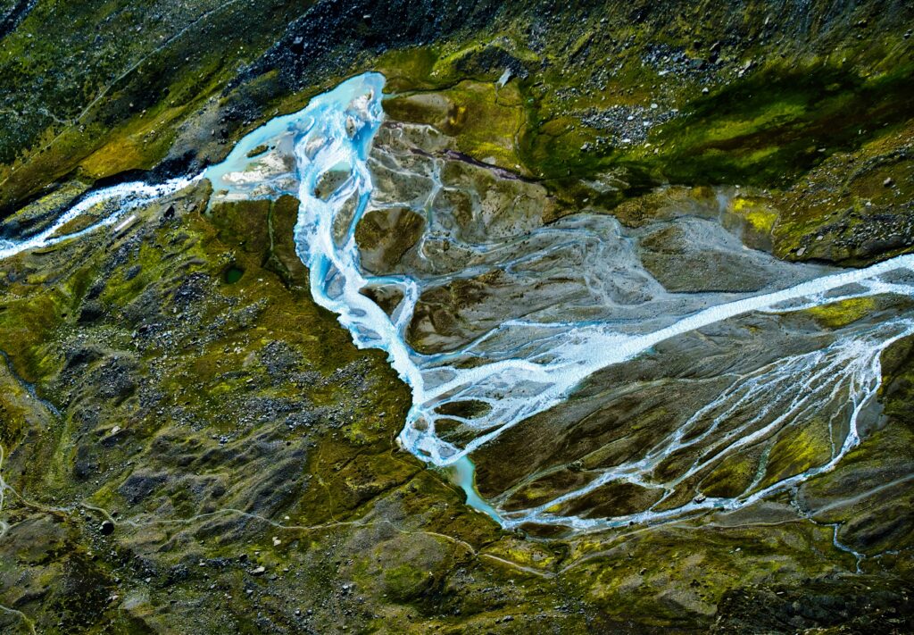 Aerial view of winding river over green rugged landscape with flowing water and natural textures Wallpaper