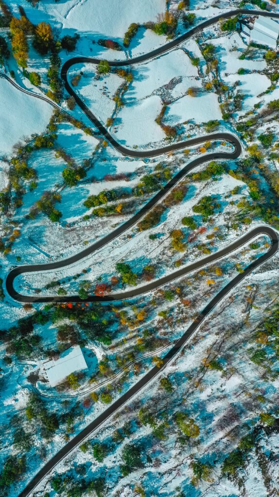 Aerial view of winding road through snowy landscape with bare trees and colorful foliage wallpaper