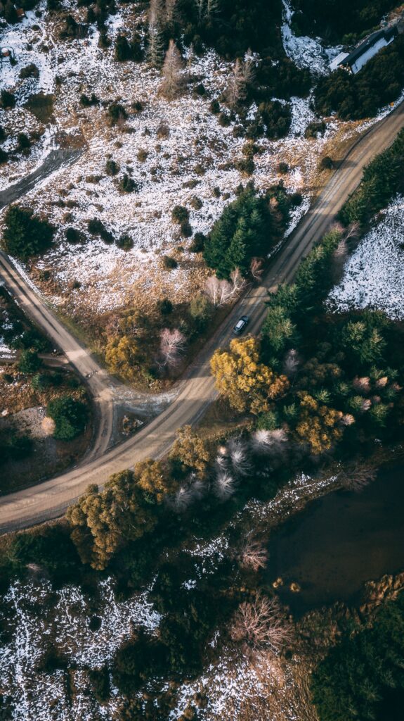 Aerial view of winding road through snowy landscape with evergreen and bare trees winter wallpaper