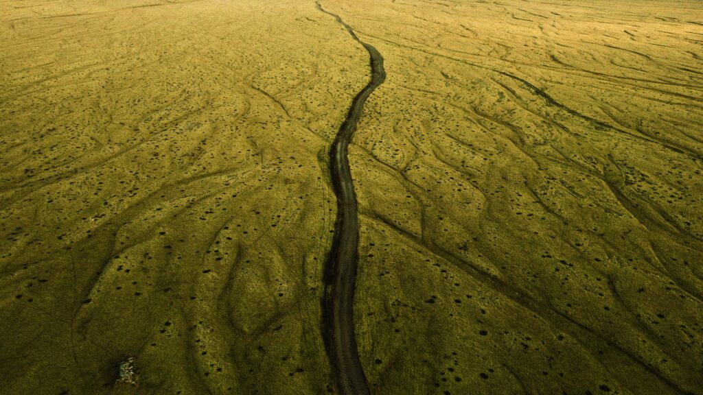 Aerial view of winding road through textured earthy brown and green natural landscape wallpaper background