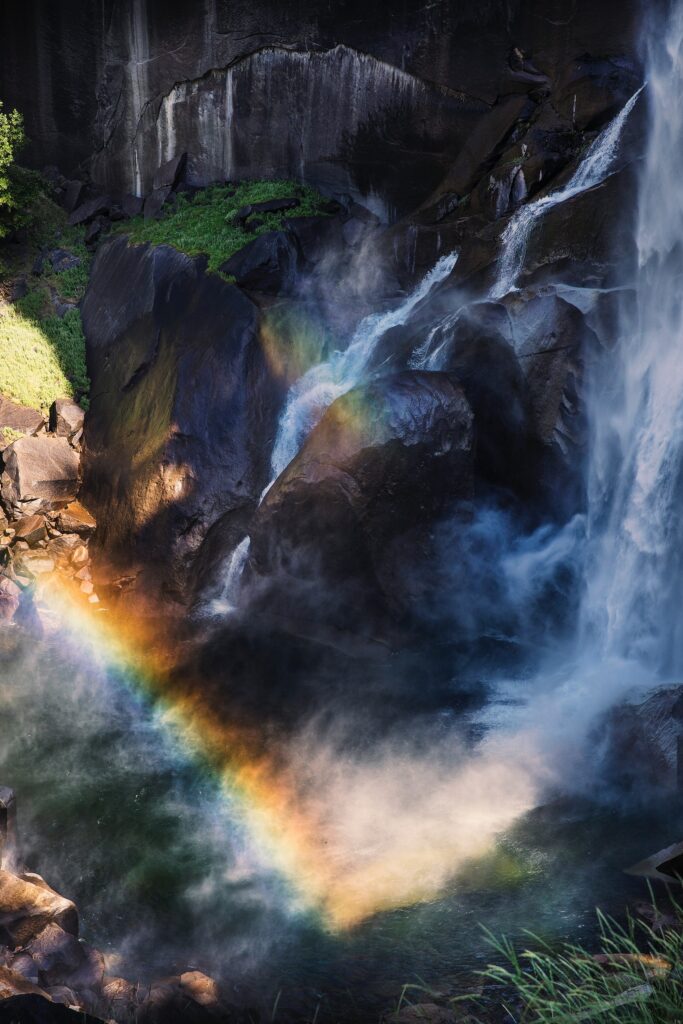 Aerial view of waterfall over cliffs with mist and rainbow vibrant blue and green nature wallpaper