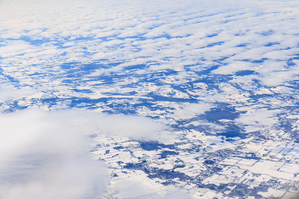 Aerial view of snow-covered fields and roads with soft clouds in a serene winter landscape wallpaper
