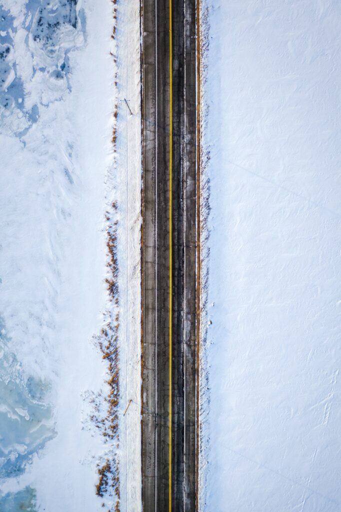 Aerial view of a straight road with yellow markings cutting through a snowy white landscape winter wallpaper background