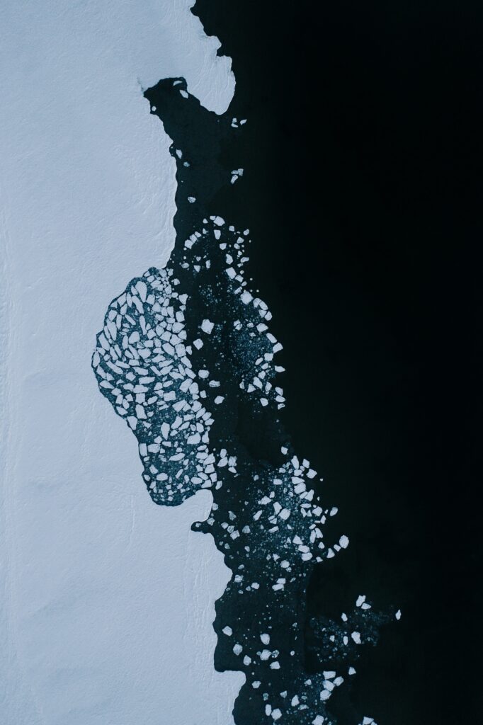 Aerial winter scene with floating ice fragments on dark water and a frozen shoreline background Wallpaper