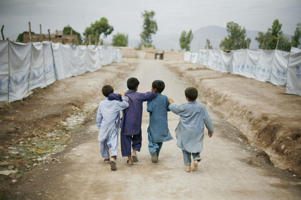 Four Afghan children walk together on dusty path arms linked showing friendship and resilience Wallpaper
