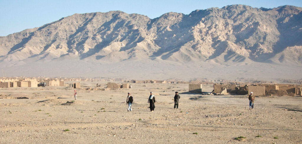 Vast Afghan desert landscape with rugged mountains and people walking across arid terrain wallpaper
