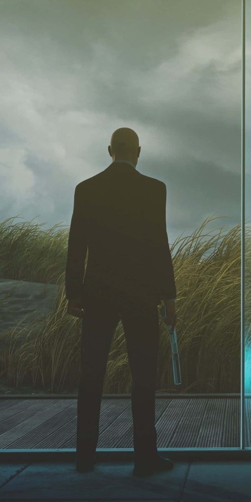 Agent 47 in black suit with Silverballer pistol against moody overcast landscape wallpaper