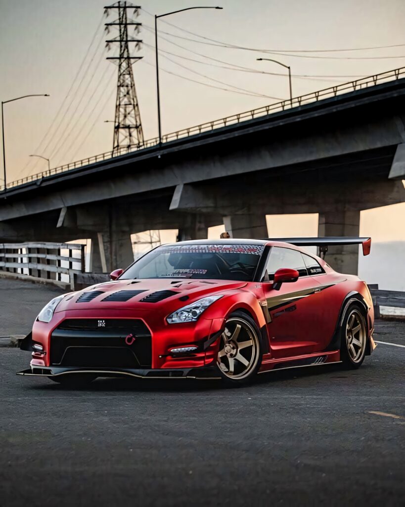 Red Nissan R35 GTR with aggressive body kit and bold rear wing parked under overpass at dusk Wallpaper