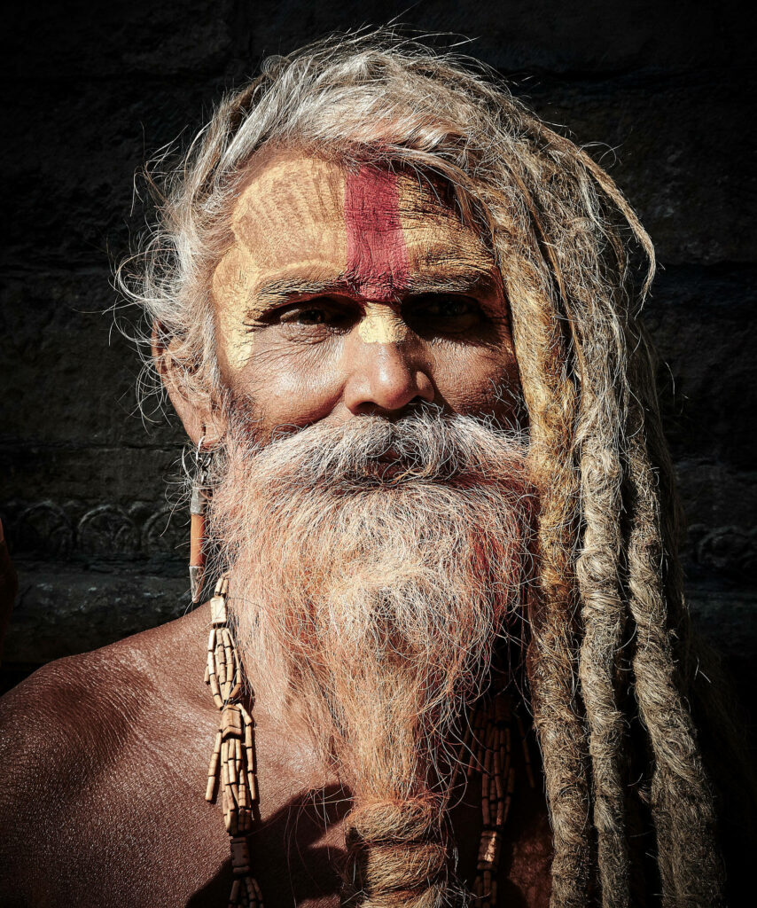 Close-up of Aghori mystic with intricate facial paint dreadlocks and traditional beads dark background Wallpaper