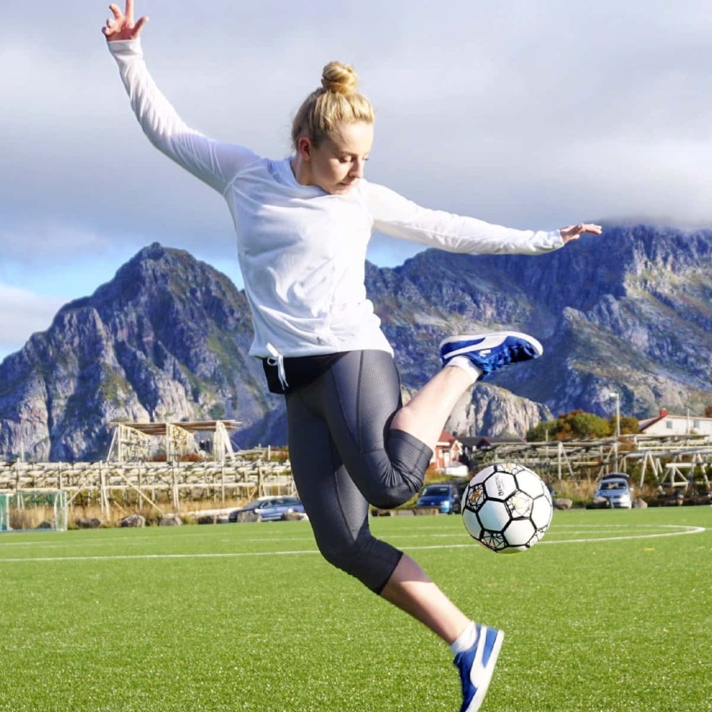 Freestyle footballer Aguska Mnich performs trick on turf field with Norwegian mountains backdrop Wallpaper