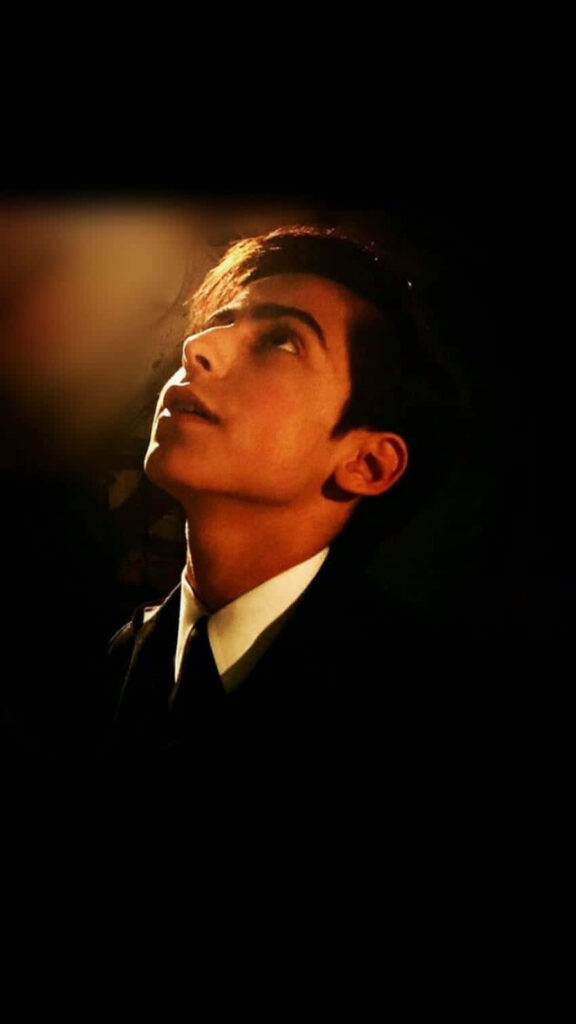 Aidan Gallagher in sharp suit and tie looking upward dramatic thoughtful dark background wallpaper
