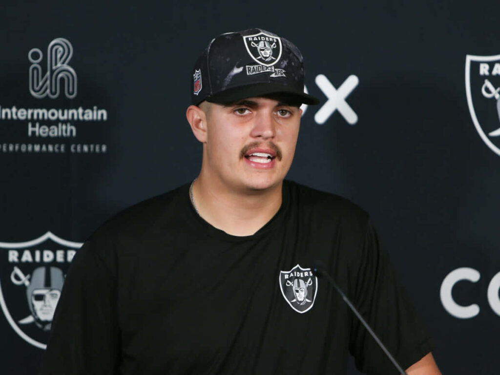 Aidan O'Connell speaking at Raiders press conference wearing team gear on wallpaper background