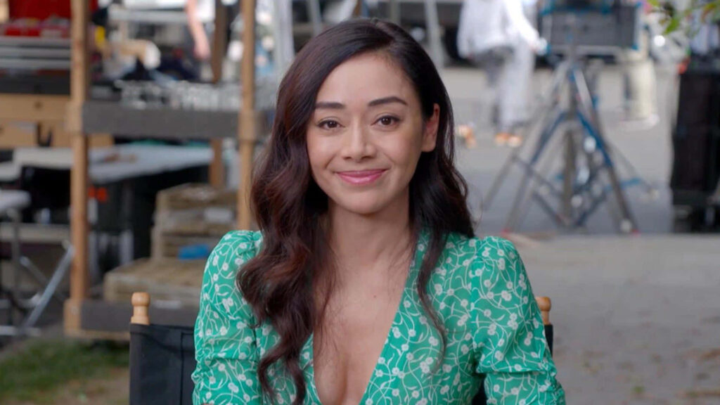 Aimee Garcia outdoors smiling wearing green patterned dress with loose wavy hair wallpaper background