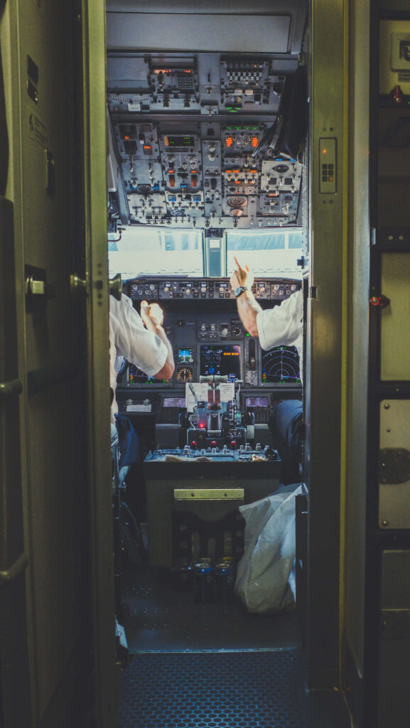 Airplane cockpit interior with illuminated controls pilots in uniform operating aircraft in daylight Wallpaper