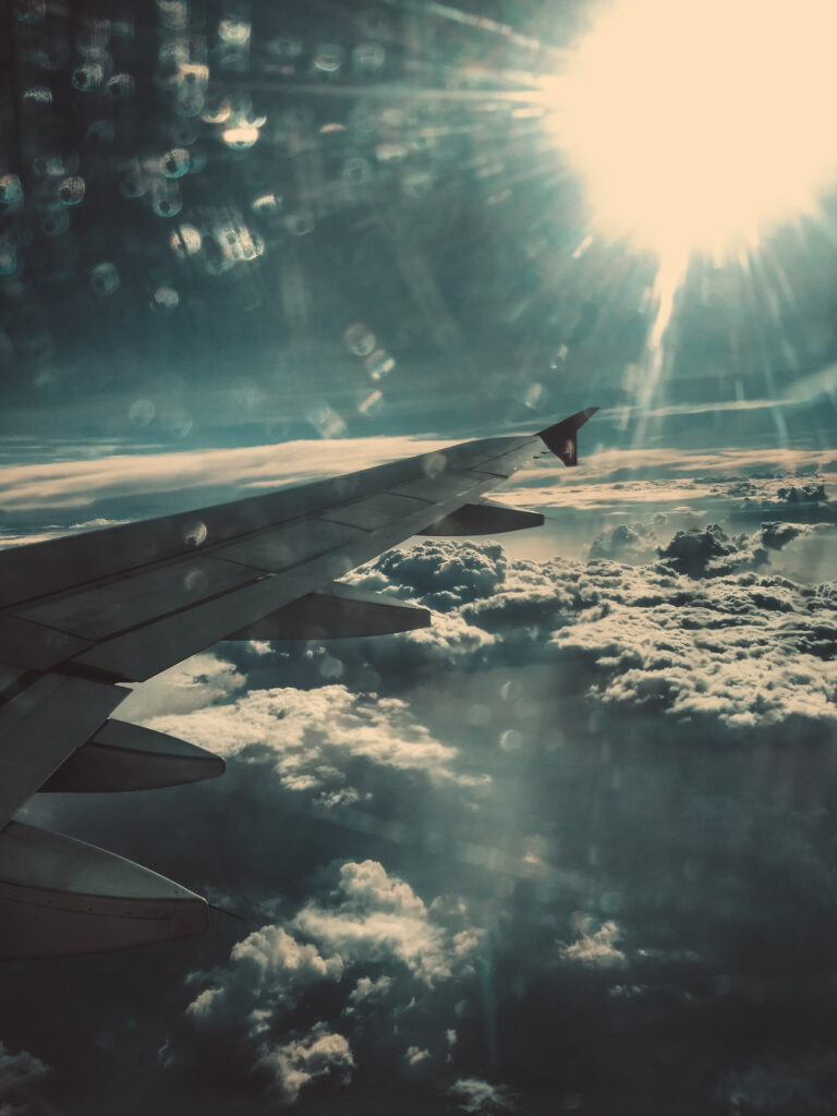 Airplane wing soaring above fluffy clouds with dramatic sunlight and lens flare wallpaper background