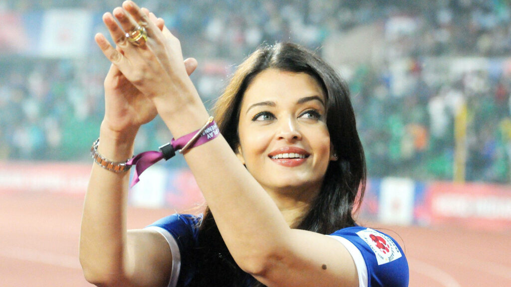 Aishwarya Rai smiling and clapping joyfully in a vibrant stadium celebrating success wallpaper
